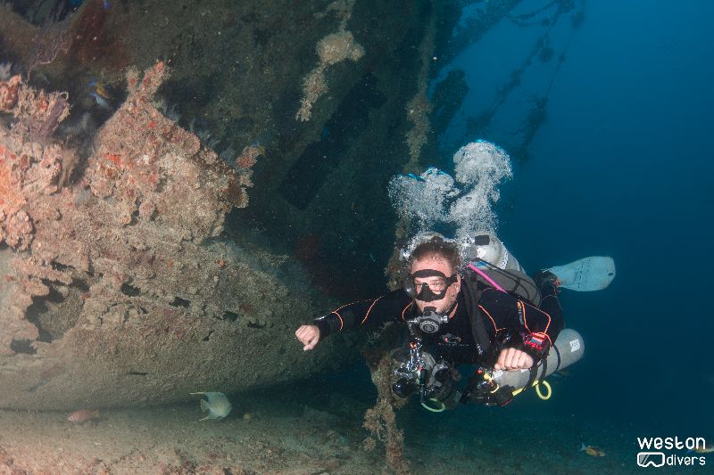 Imor - A diver swims at the sand level next to the wreck